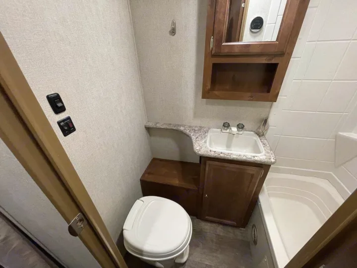 Compact RV rental bathroom featuring a toilet, sink, mirrored cabinet, and small tub/shower, ready for your travels.. gulfstream Streamlite 2016