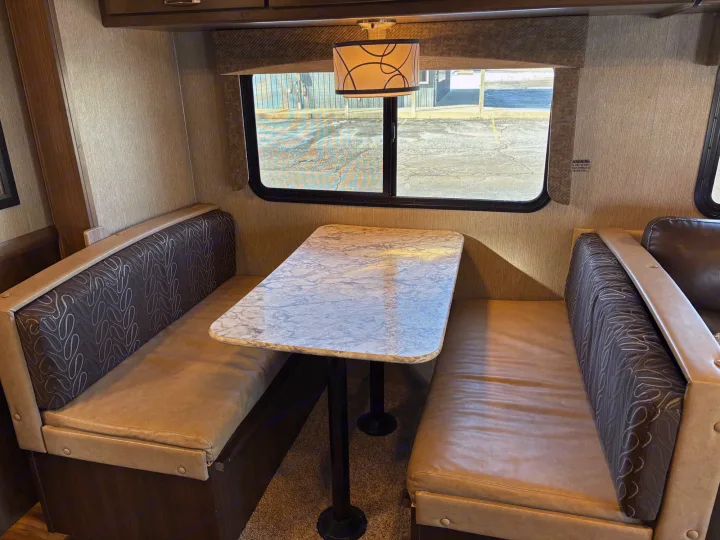 Spacious RV rental interior featuring a comfortable dinette area with a marble-look table and bench seating, ideal for dining.. Nexus RV Triumph 2021