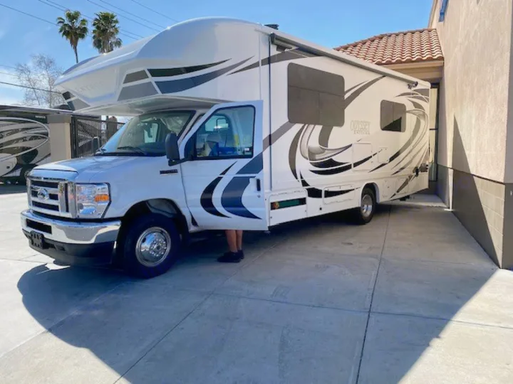 White Class C RV rental with graphic decals, parked on concrete. A person is getting in/out, ready for adventure.. Entegra Coach Odyssey 2021