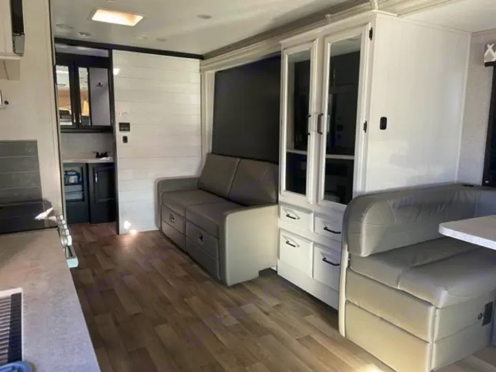 An RV rental's spacious living area with a gray sofa, white cabinets, dining booth, and wood-look floor.. Entegra Coach Odyssey 2021
