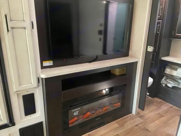 Modern RV rental interior with a wall-mounted TV, electric fireplace, and built-in storage. Bathroom visible through doorway.. Entegra Coach Odyssey 2021