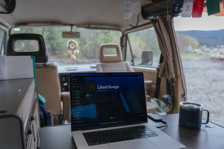 Inside an RV rental: a laptop displays Spotify, a Yeti mug sits on a table. A cozy mobile office with nature views.. Volkswagen Westfalia 1989