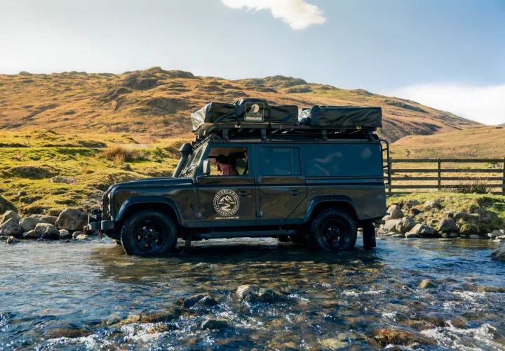 Adventure RV rental: A black Land Rover Defender 4x4 fording a stream, equipped for overland camping in the mountains.. Land Rover Defender 110 XS Utility + 2 Roof Tents 2013