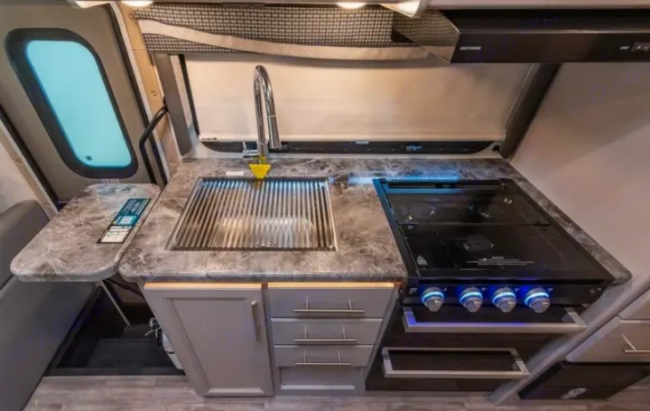 A compact RV rental kitchen area featuring a sink, stove, and marbled countertop with cabinets.. Thor Outlaw 2024