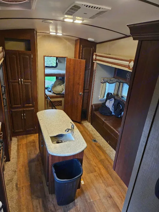 Inside an RV rental showing a full kitchen island, wood floors, bunk beds, and a sofa lounge area.. Keystone Outback 2016