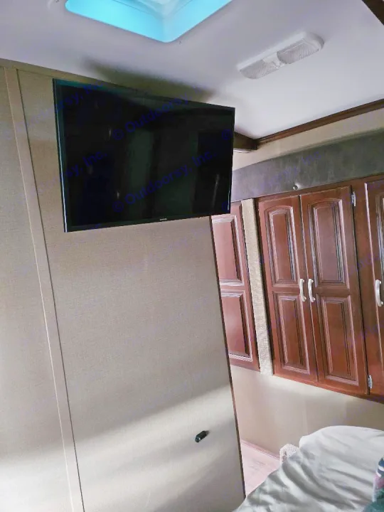 Inside an RV rental: a bedroom with wall-mounted TV, wood cabinets, skylight, and compact design.. Keystone Outback 2016