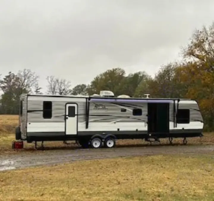 Grey and white RV rental, with an extended awning, set up in a grassy field, ready for outdoor living or travel.. Jayco Jay Flight 2018