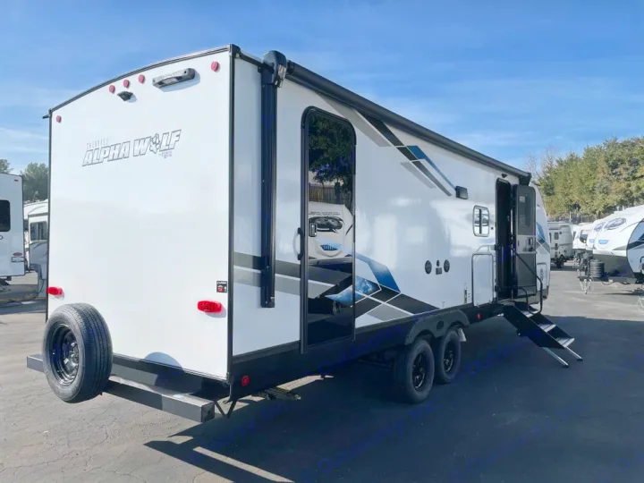 White Alpha Wolf travel trailer, a featured RV rental. Showing extended steps, awning, and rear spare tire.. Forest River ALPHA WOLF 26DBH-L 2024