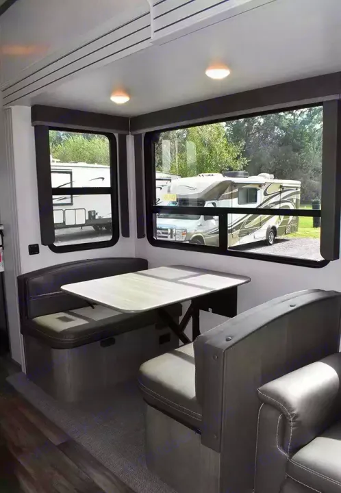 Cozy RV rental dinette with comfortable bench seating, a light wood table, and large windows offering views outside.. Keystone Cougar 2021