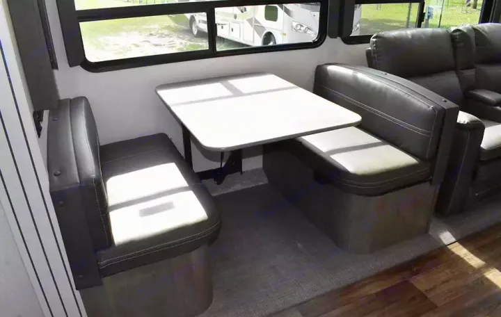 This **RV rental** interior features a comfy dinette with dark gray booth seating and a white table, alongside plush theater seats.. Keystone Cougar 2021