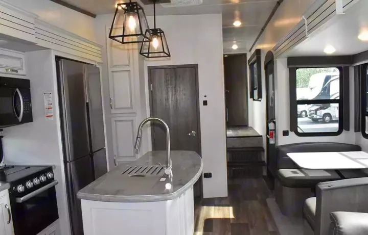 Inside a modern RV rental: well-equipped kitchen with island, adjacent dinette, and rear steps leading to private areas.. Keystone Cougar 2021