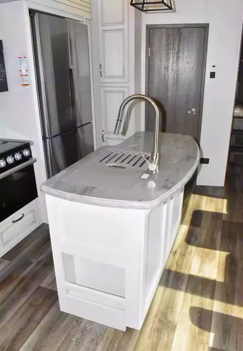 Modern RV rental kitchen interior featuring a white island with sink, stainless steel refrigerator, and oven.. Keystone Cougar 2021