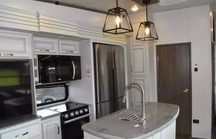 Modern RV rental kitchen with stainless steel appliances, island, and stylish pendant lighting. Ready for your adventure.. Keystone Cougar 2021