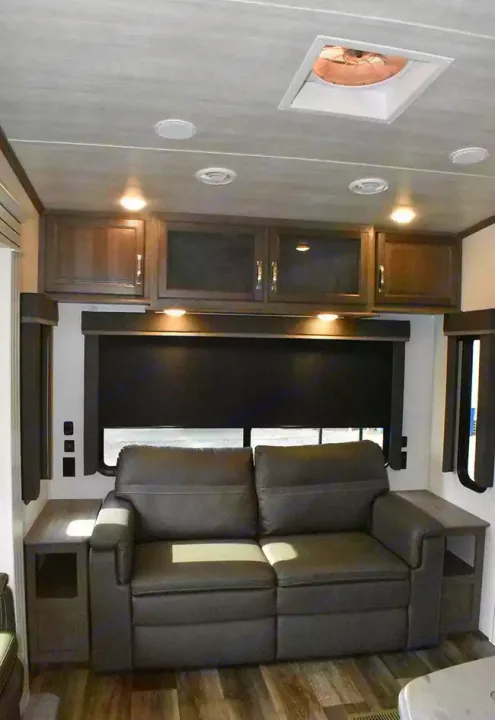 Cozy RV rental living area featuring a comfortable reclining sofa, overhead storage, and large windows.. Keystone Cougar 2021