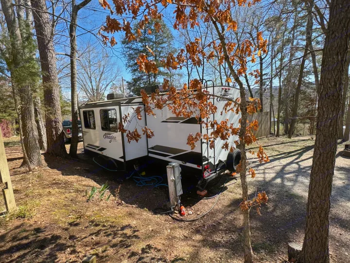 RV rental ready for adventure at a wooded campsite, showing utility hookups under sunny skies.. Grand Design Imagine 2019