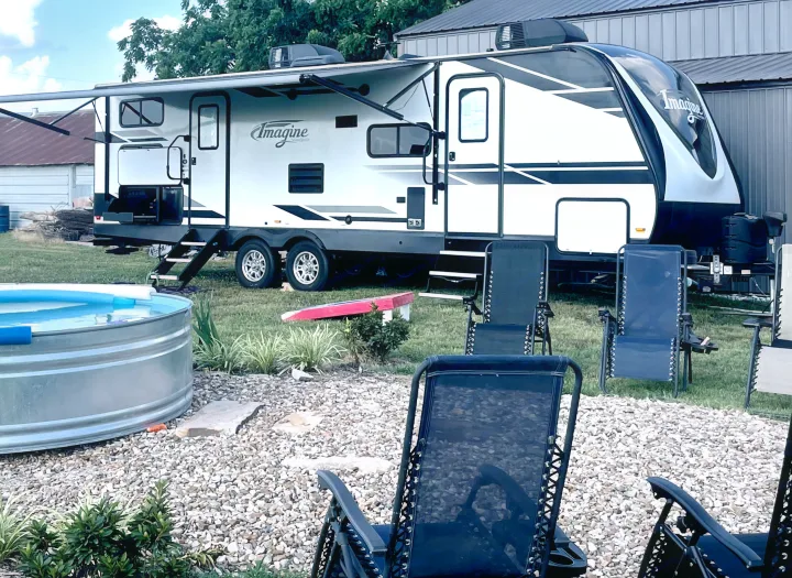 Imagine travel trailer RV rental with extended awning, small pool, and outdoor chairs on a gravel patio.. Grand Design Imagine 2019