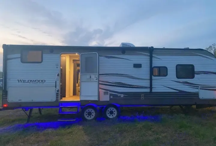 Experience an RV rental! This modern travel trailer features blue underglow and inviting interior lights at dusk.. Forest River Wildwood 2018