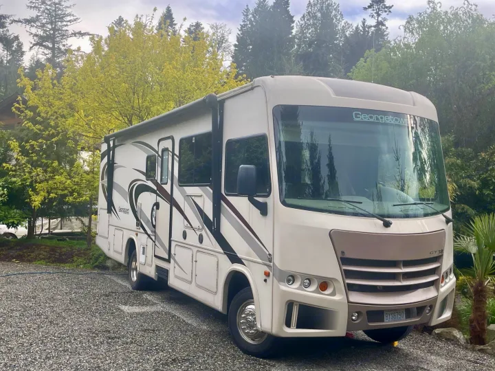 A light-colored Georgetown Class A RV rental is parked on gravel in a green, wooded area.. Georgetown GT3 2016