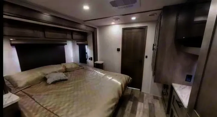Comfortable RV rental bedroom featuring a large bed, overhead cabinets, and wood-look flooring.. FR3 FR3 Motorhome 2023