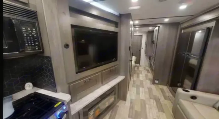 Modern RV rental interior: kitchen with microwave/stove, living area with TV, fireplace, and hallway with fridge.. FR3 FR3 Motorhome 2023