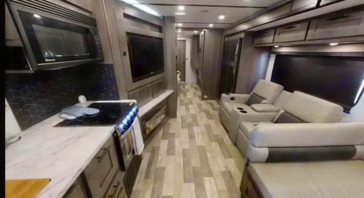 Experience a spacious RV rental interior! This modern setup features a full kitchen with a stove/microwave, comfy living area with recliners, and wood-look flooring, extending to a rear hallway.. FR3 FR3 Motorhome 2023