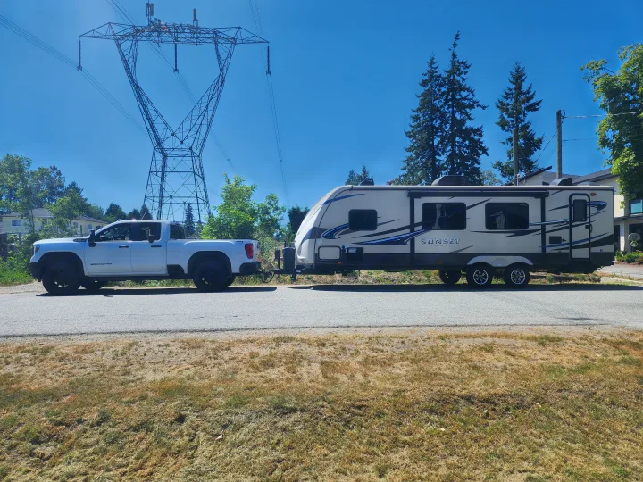 White GMC pickup truck towing a Sunset Trail RV rental. Parked on a sunny day with power lines and trees in the background.. Crossroads Sunset Trail 2015