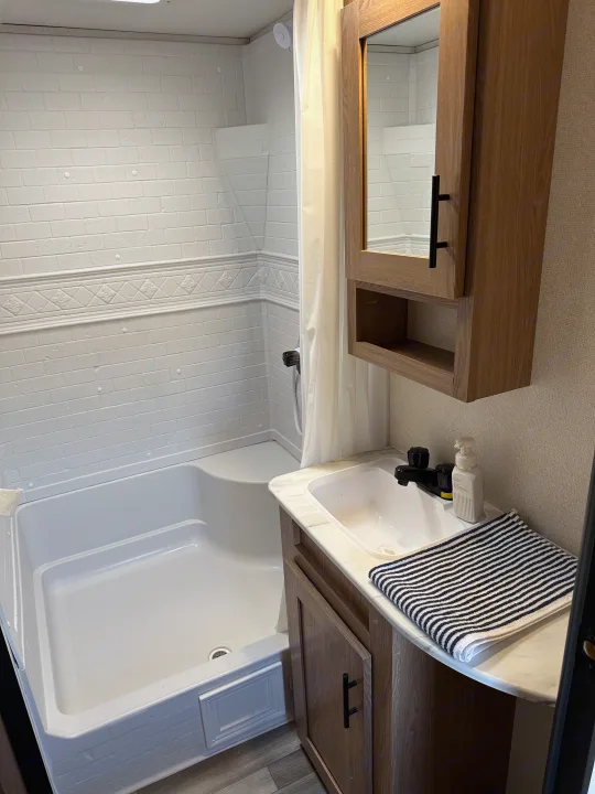 Clean RV rental bathroom features a compact tub/shower with brick-patterned walls, modern sink, and wood vanity.. Forest River Avenger 2023