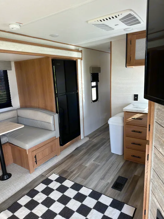 Inside an RV rental: dinette seating, a full-size refrigerator, kitchen counter, and modern flooring with a checkered rug.. Forest River Avenger 2023