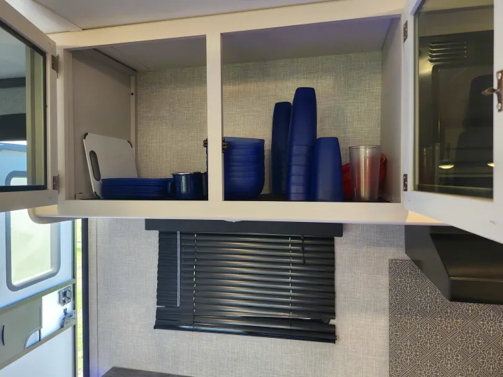 Organized kitchen cabinet in an RV rental, featuring blue dishes and a cutting board.. Crossroads RV Volante 2022