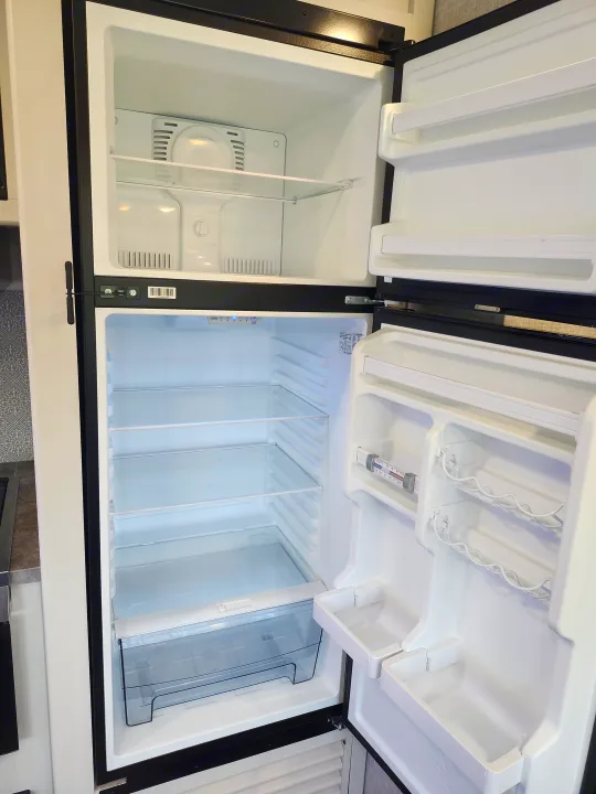 An open, empty refrigerator within an RV rental, featuring a top freezer, main fridge compartment with glass shelves, and door storage.. Crossroads RV Volante 2022