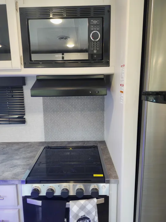 Well-equipped RV rental kitchen featuring a Greystone microwave, range hood, and stove/oven for travelers.. Crossroads RV Volante 2022