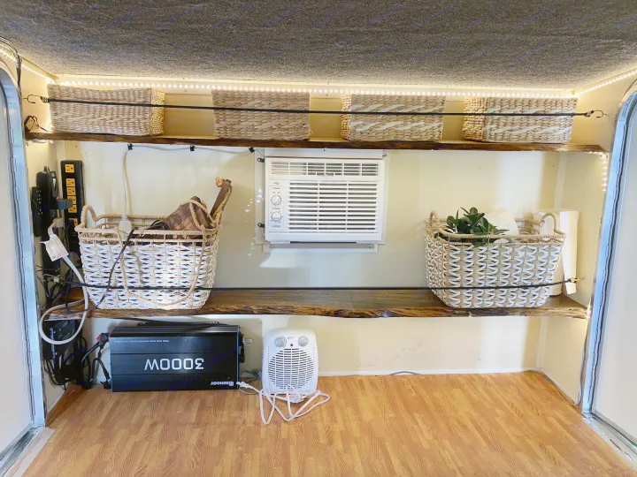 Cozy RV rental interior with organized storage, AC, and lighting, featuring wood shelves, wicker baskets, and a power setup.. Runaway Campers Rangerunner 2021