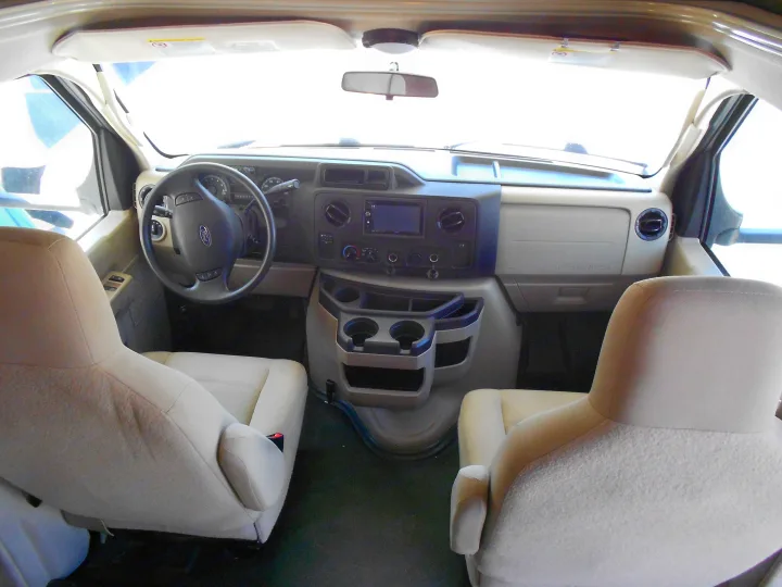 Spacious RV rental front cab interior view, featuring beige seats, dashboard, steering wheel, and windshield.. Coachmen Freelander 2018
