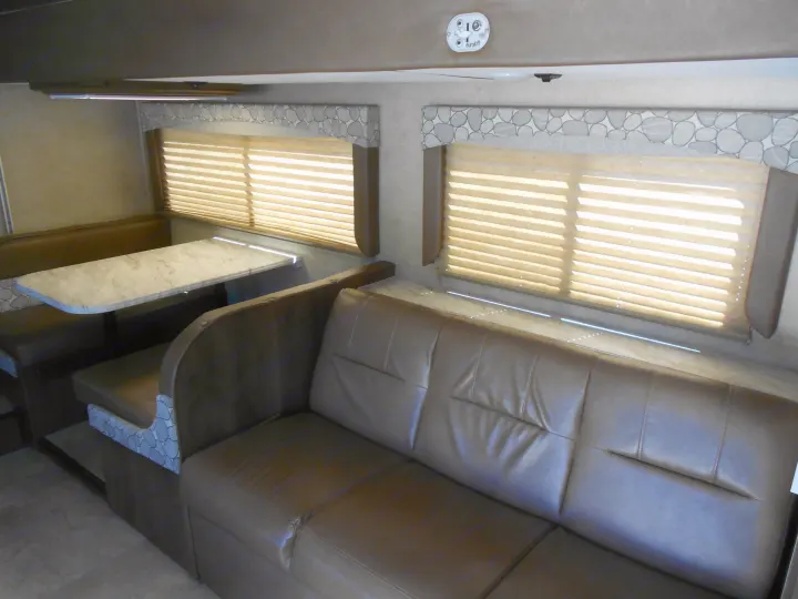 Spacious RV rental interior with a long brown leather-look sofa and a brown dinette with a light-colored table. Ideal for living.. Coachmen Freelander 2018