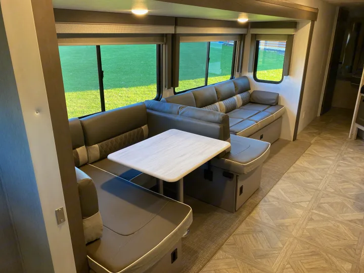 RV rental: Spacious, modern RV interior with an L-shaped dinette, sofa, and large windows showing green grass.. Forest River Salem 2024