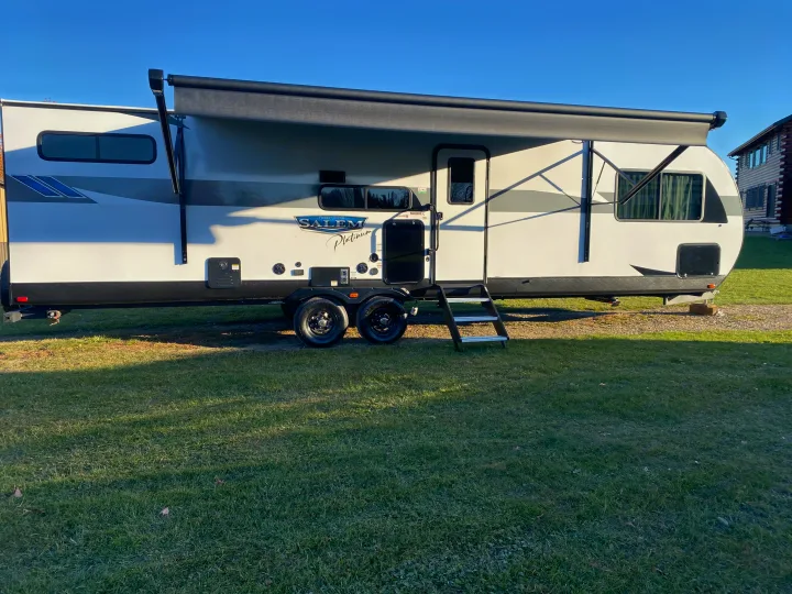 A white and grey Salem Platinum travel trailer, an ideal RV rental, parked outdoors with its awning extended and steps down.. Forest River Salem 2024