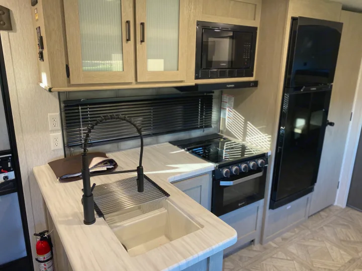 Modern RV rental kitchen featuring a large sink with pull-down faucet, black stove/oven, microwave, and refrigerator.. Forest River Salem 2024