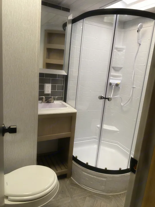 Inside an RV rental: a modern, compact bathroom with curved shower, sink vanity, and toilet.. Forest River Salem 2024