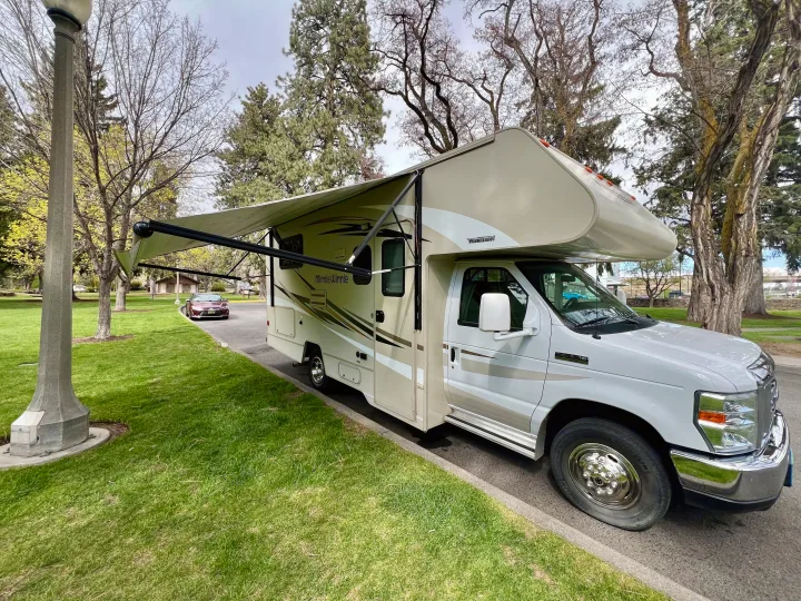 An RV rental adventure awaits! A Winnebago Minnie Winnie motorhome, awning extended, parked roadside in a park.. Winnebago Minnie Winnie 2017