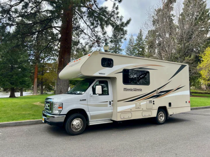 Winnebago Minnie Winnie RV rental parked on asphalt, with trees and a river in the background. Ready for your camping vacation.. Winnebago Minnie Winnie 2017