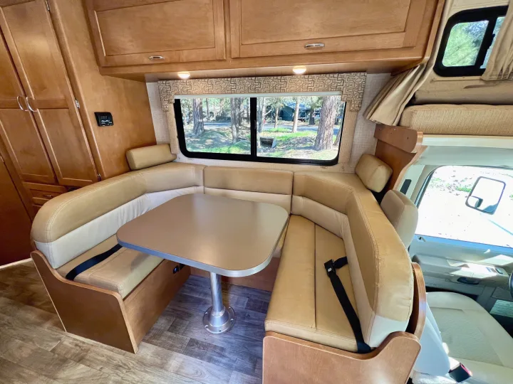 RV rental interior, showing the U-shaped dinette with table, plush seating, and overhead wooden cabinetry.. Winnebago Minnie Winnie 2017