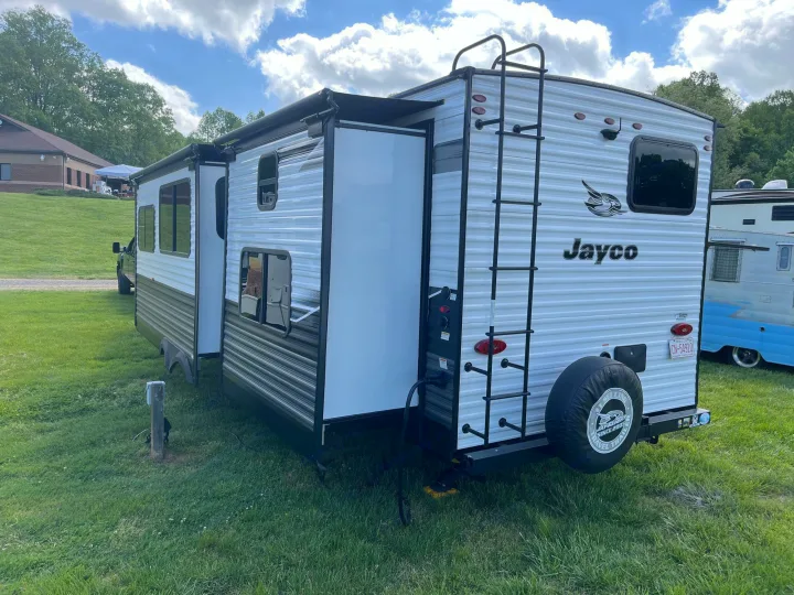 This Jayco travel trailer, ideal for an rv rental, is parked on grass with its slide-out extended at a campground.. Jayco Jay Flight 2022