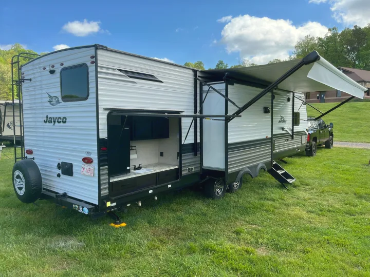 A large grey and white Jayco travel trailer with an extended awning and outdoor kitchen, set on green grass. Ideal for an RV rental.. Jayco Jay Flight 2022