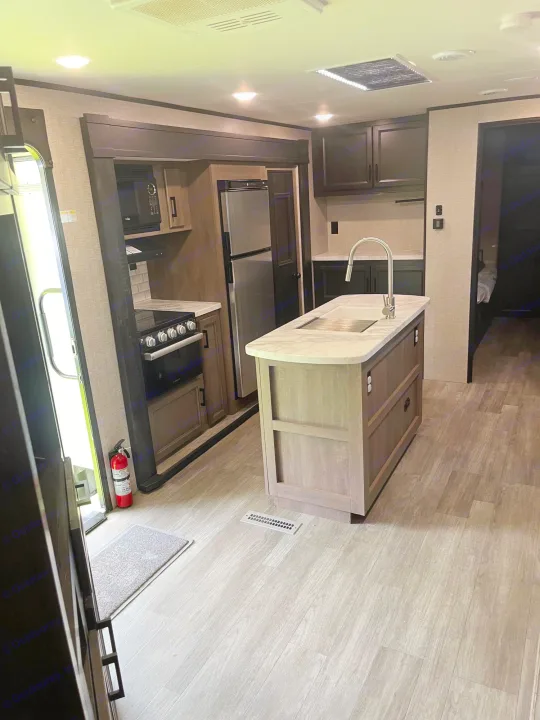 RV rental kitchen interior featuring a stove, fridge, island with sink, and modern cabinetry. Perfect mobile home for travel.. Jayco Jay Flight 2022