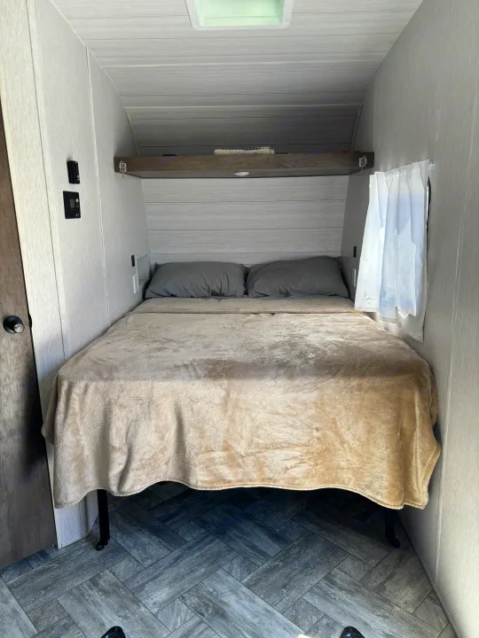Inside a compact RV rental: a modern bedroom with a comfortable bed, light paneling, and gray herringbone flooring.. Forest River Stealth 2022