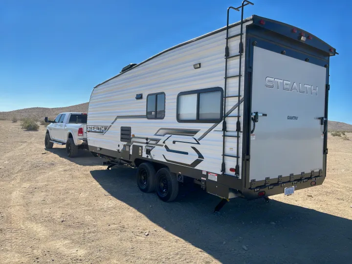 A white pickup truck tows a large Stealth RV rental (travel trailer) through a vast, sunny desert landscape.. Forest River Stealth 2022