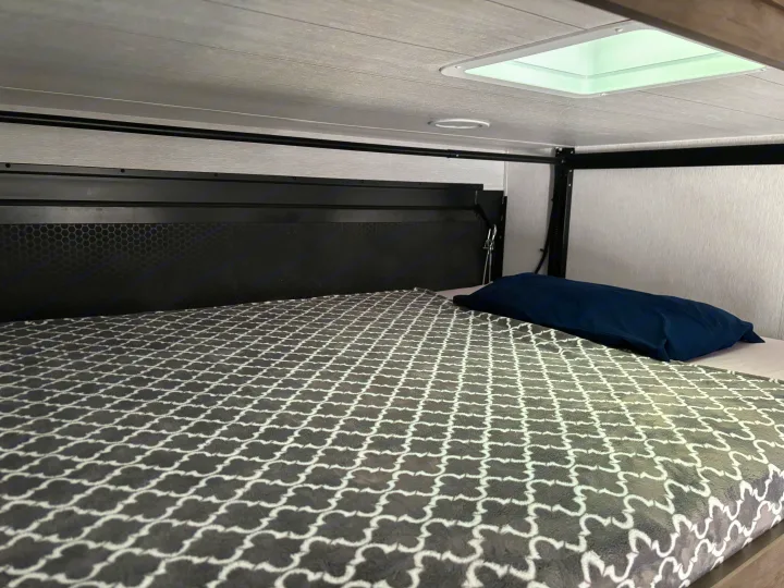 RV rental interior showing a cozy bunk bed with gray patterned blanket, blue pillow, and ceiling skylight.. Forest River Stealth 2022