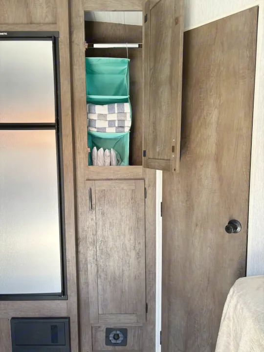 RV rental interior with efficient storage: fridge, open cabinet, teal organizer with towels, and a privacy door.. Forest River Stealth 2022