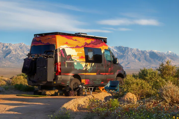 Adventure rv rental van with a vibrant mountain mural parked in a scenic desert campsite with snowy peaks.. Mercedes-Benz Sprinter 2023