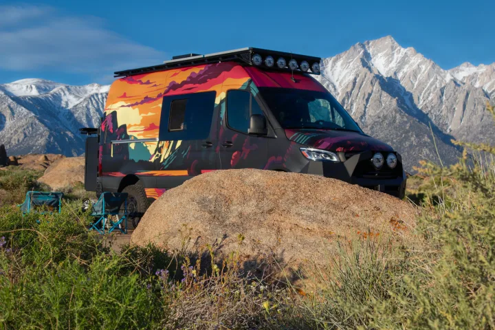 Adventure-ready RV rental van with mountain art parked amidst rocks & snow-capped peaks. Perfect for scenic road trips.. Mercedes-Benz Sprinter 2023